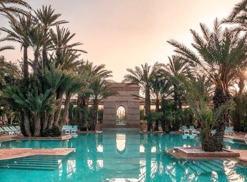 Idyllic tropical resort pool with palm trees reflecting at sunset.