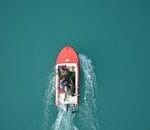 Top view of a red motorboat with fishermen navigating open turquoise waters.