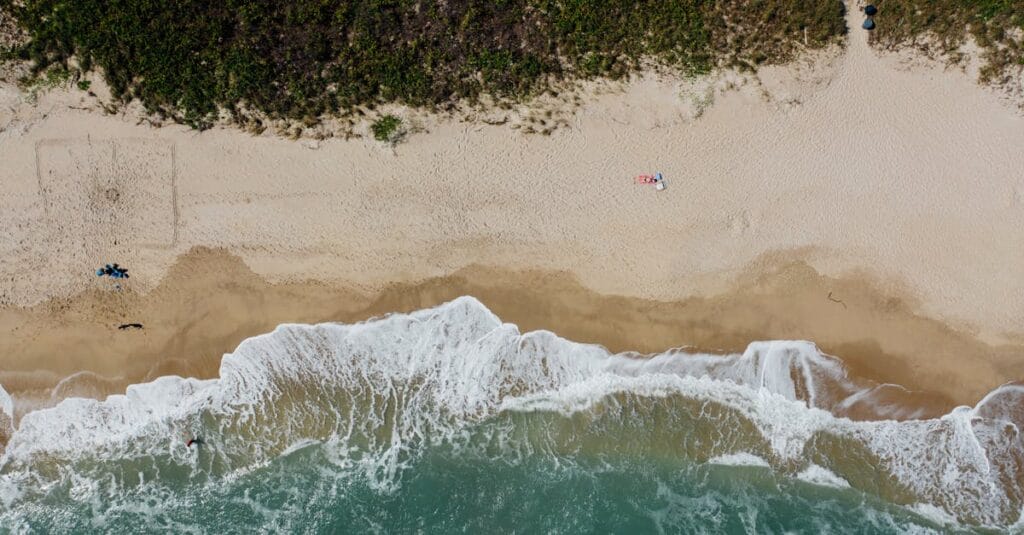 Aerial shot of a sandy beach with turquoise waves, capturing summer relaxation and coastal scenery.