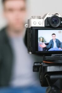 Man recording a vlog indoors using a mirrorless camera on a tripod with selective focus.