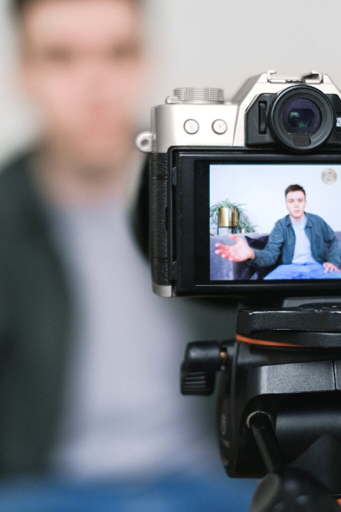 Man recording a vlog indoors using a mirrorless camera on a tripod with selective focus.