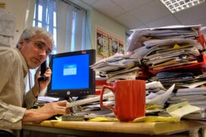 A real estate agent working late at a desk buried in paperwork and a laptop