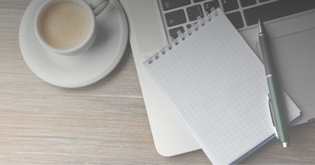 Coffee cup, spiral notepad and pen on a wooden desk, illustrating real estate brokerage culture as everyday infrastructure