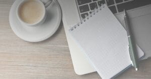 Coffee cup, spiral notepad and pen on a wooden desk, illustrating real estate brokerage culture as everyday infrastructure
